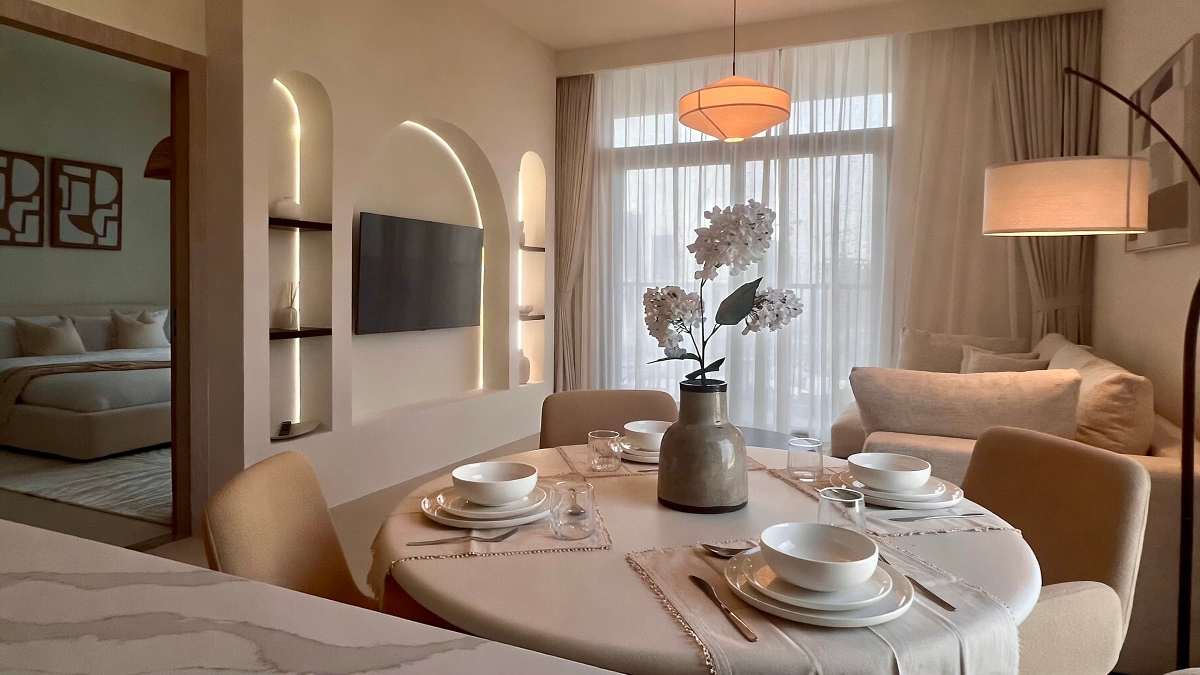 Hadley Height, the finished living room: dining table laid, lit arched niches, sheer curtains, bedroom beyond