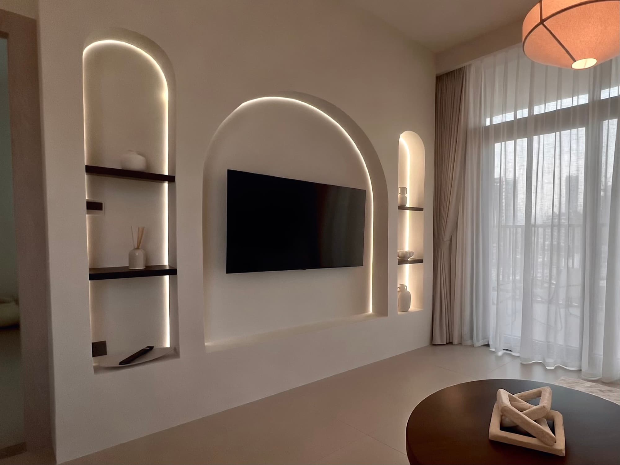Hadley Height, the same living room finished: lit arched niches, sheer curtains, dark wood coffee table